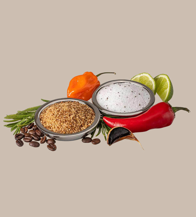 Two small bowls with spices, surrounded by peppers, limes, and coffee beans on a beige background