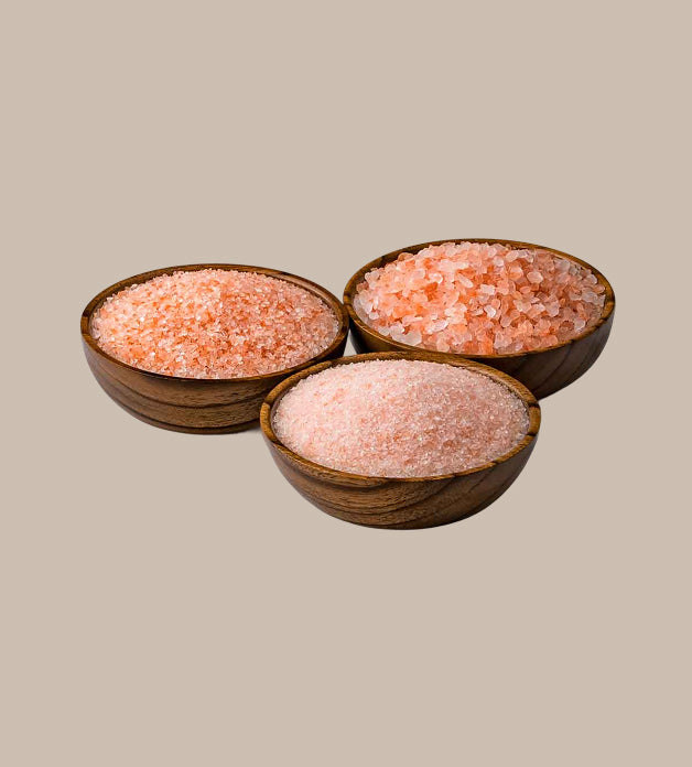 Three wooden bowls filled with pink himalayan salt on a beige background
