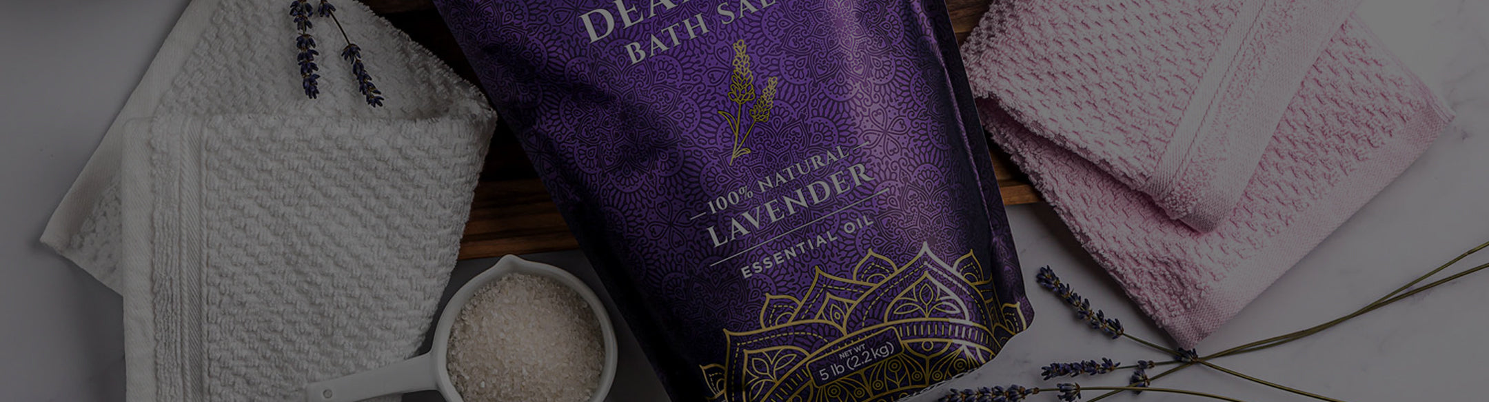 Bath salt package with lavender oil on a wooden surface with towels and lavender flowers.