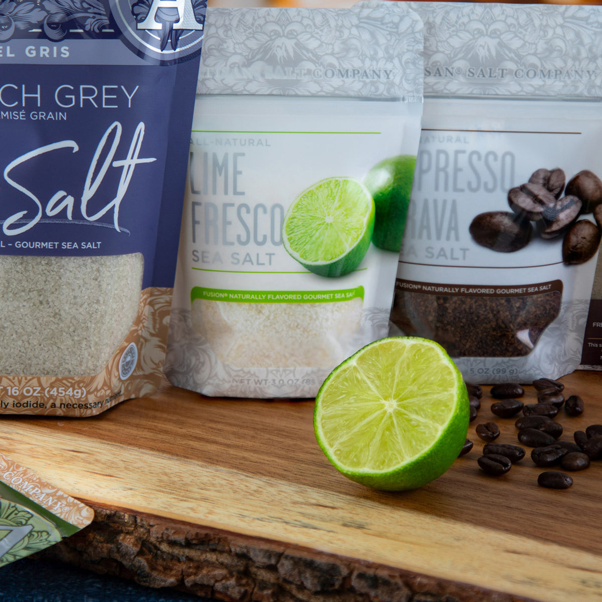 Three salt packages with a lime and coffee beans on a wooden surface