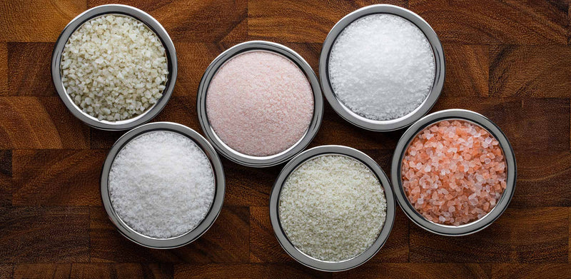 Assorted salts in stainless steel bowls on wooden table