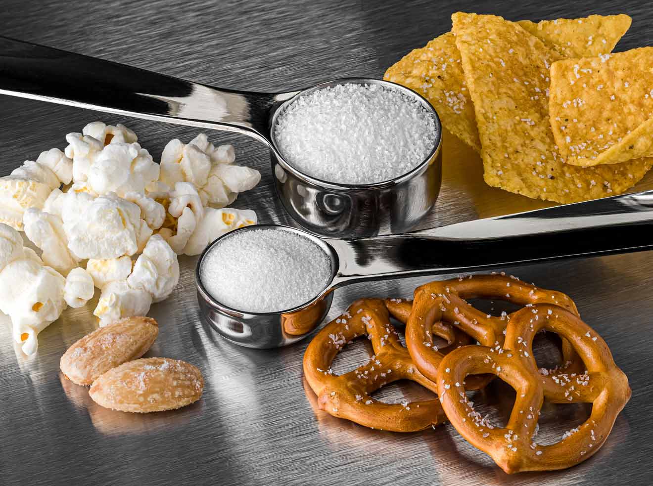 Pacific Blue sea salt in measuring cups next to snacks on stainless steel surface