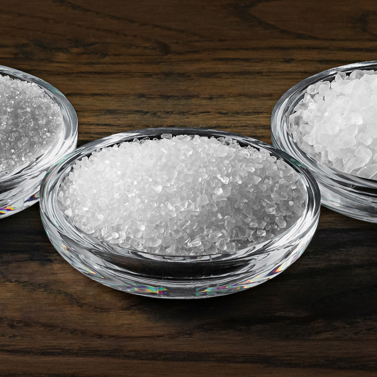 Three glass bowls filled with white granulated sugar on a wooden surface