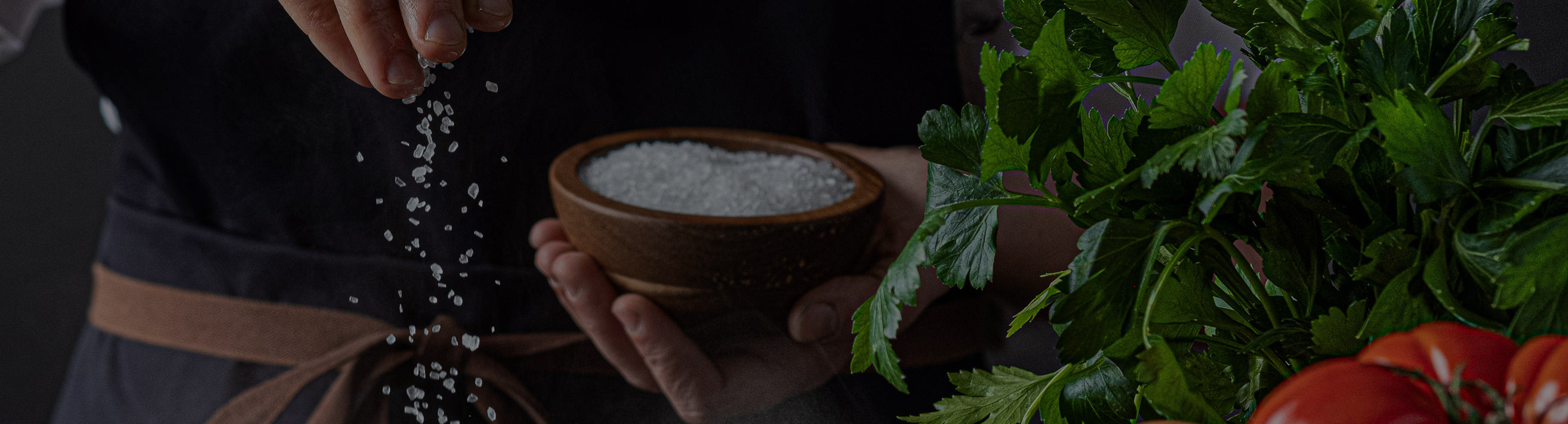 Person holding a container of salt with fresh vegetables in the background