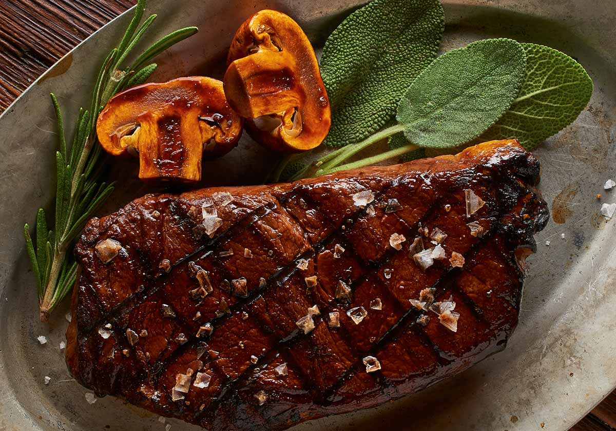 Grilled steak on a metal plate with rosemary and coffee beans on a wooden surface