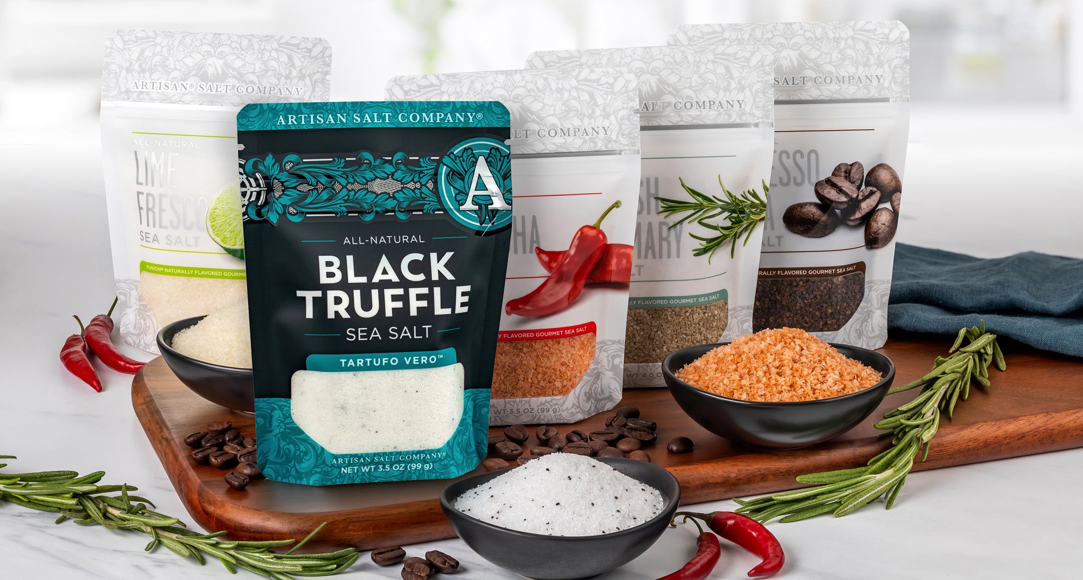 Assorted salt products including Black Truffle sea salt on a wooden board with herbs and spices.
