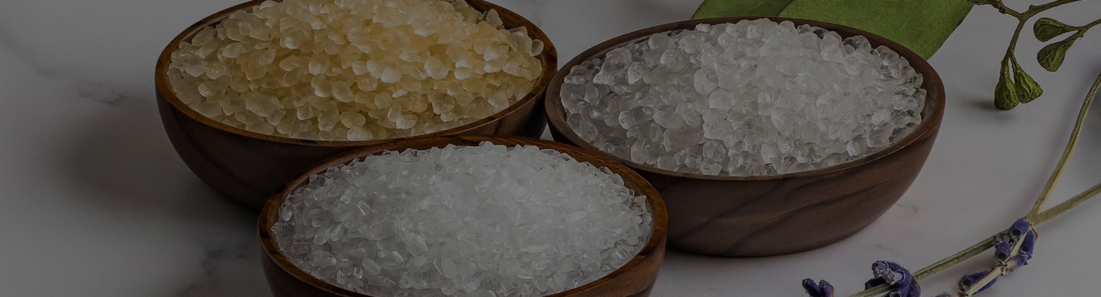 Three wooden bowls containing different types of sugar on a marble surface.