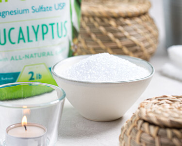 Bowls of Eucalyptus Ultra Epsom salt next to packaged product and candle