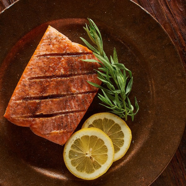 Salmon fillet with lemon slices and herbs on a wooden plate