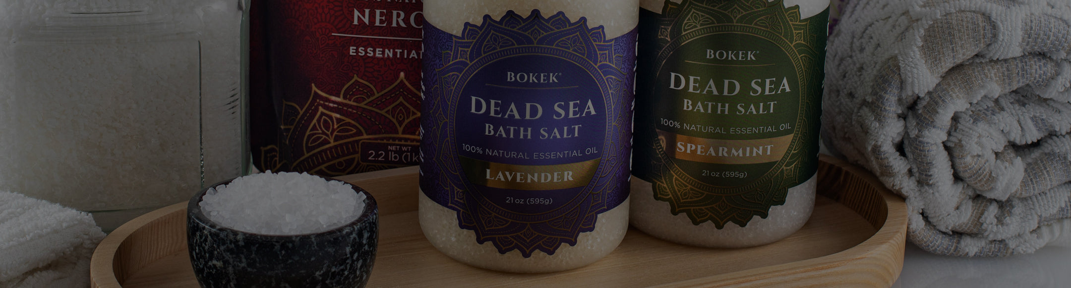 Dead Sea bath salt products on a wooden tray with towels and a bottle in the background.