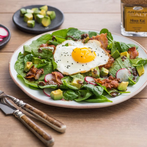 Salad with a fried egg on a wooden table with utensils and a bottle of dressing.