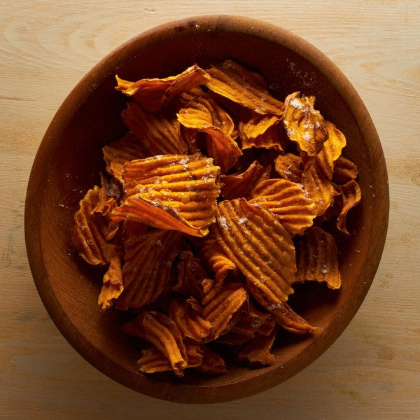 Wooden bowl filled with ruffled potato chips on a wooden surface