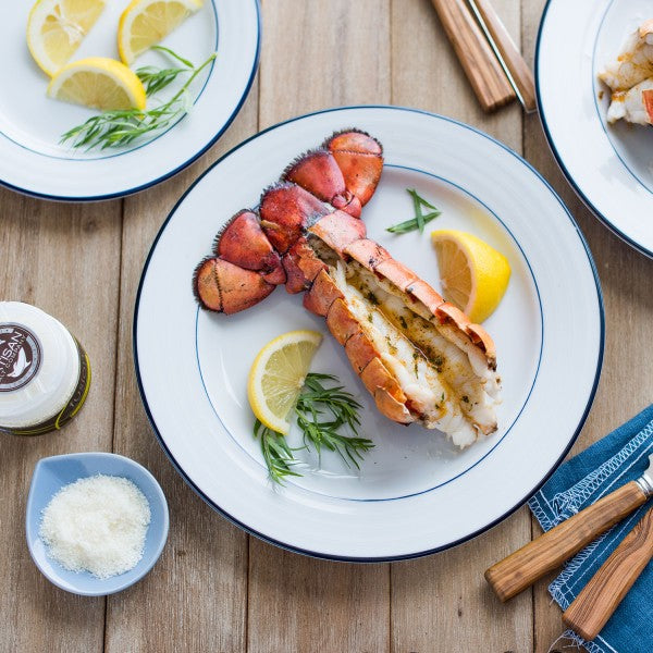 Lobster tail on a plate with lemon and herbs on a wooden table