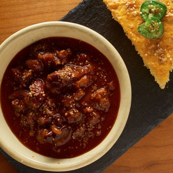 Bowl of chili with a side of cornbread on a wooden surface
