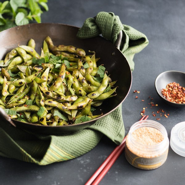 Green bean dish in a black bowl with red pepper flakes on a dark surface