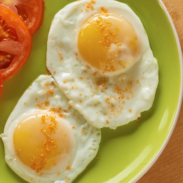 Two fried eggs with a sprinkle of flavored salt on a green plate with tomato slices.