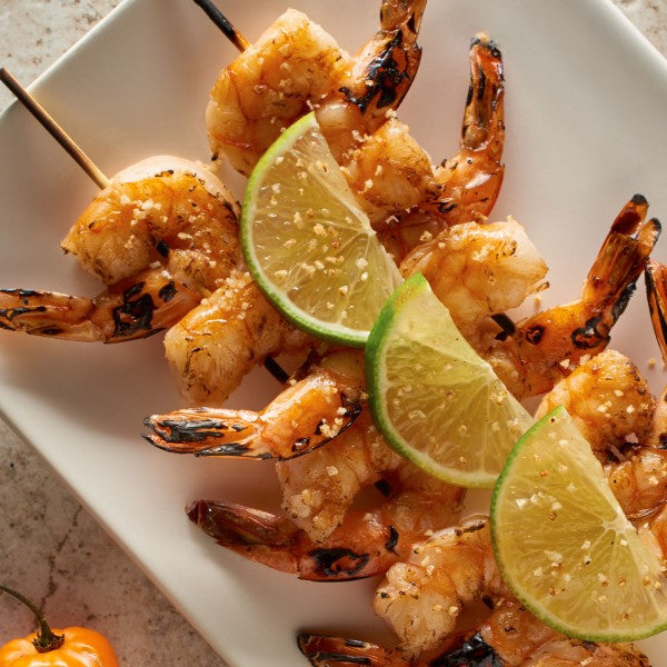 Grilled shrimp skewers with lime wedges on a white plate