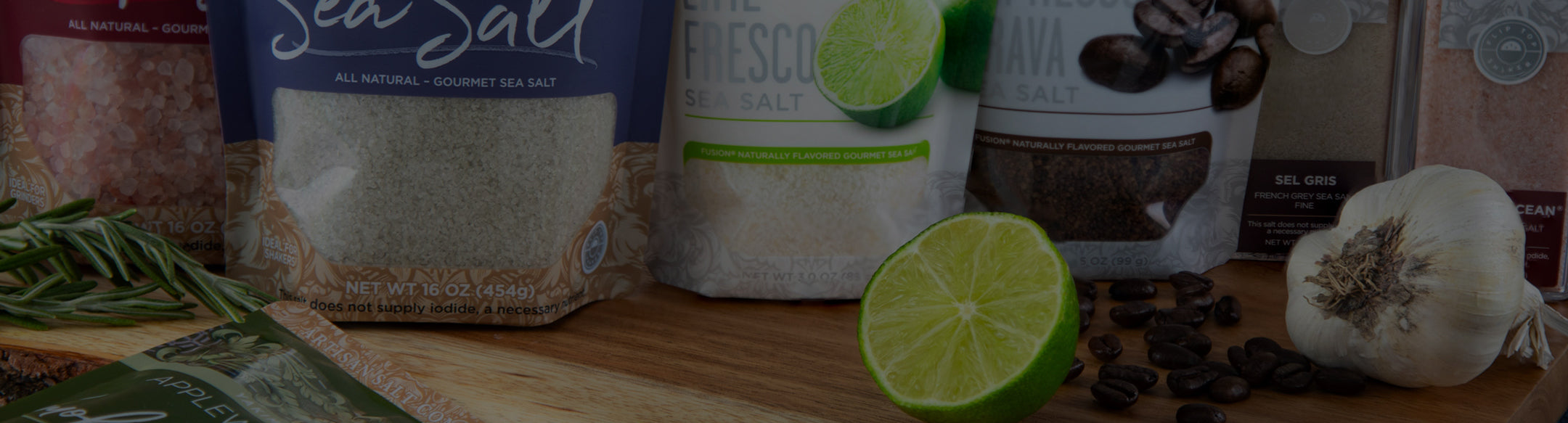 Assorted food items including a bag of sea salt, a container of coffee, and limes on a wooden surface.
