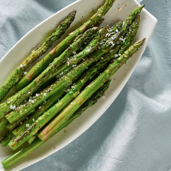 Roasted asparagus on a white plate with a light blue background