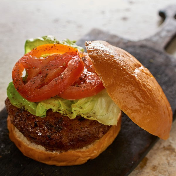Close-up of a burger with tomato slices and lettuce on a wooden surface