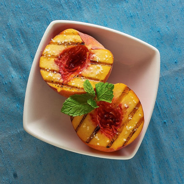Grilled peaches with mint leaves on a white plate against a blue background