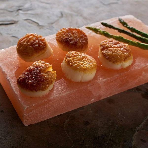 Seared scallops on a pink salt block with asparagus on a stone surface