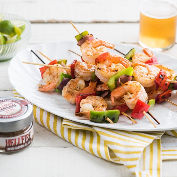 Shrimp skewers with vegetables on a plate with Hellfire pepper sauce and a glass of beer.