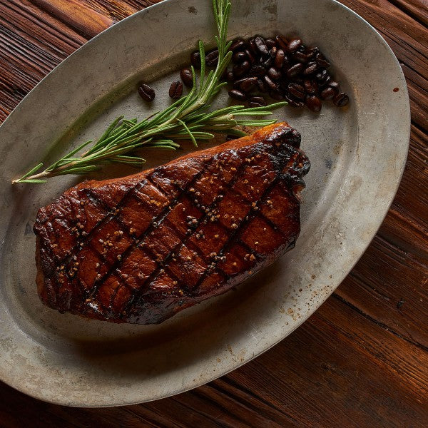 Grilled steak on a metal plate with rosemary and coffee beans on a wooden surface