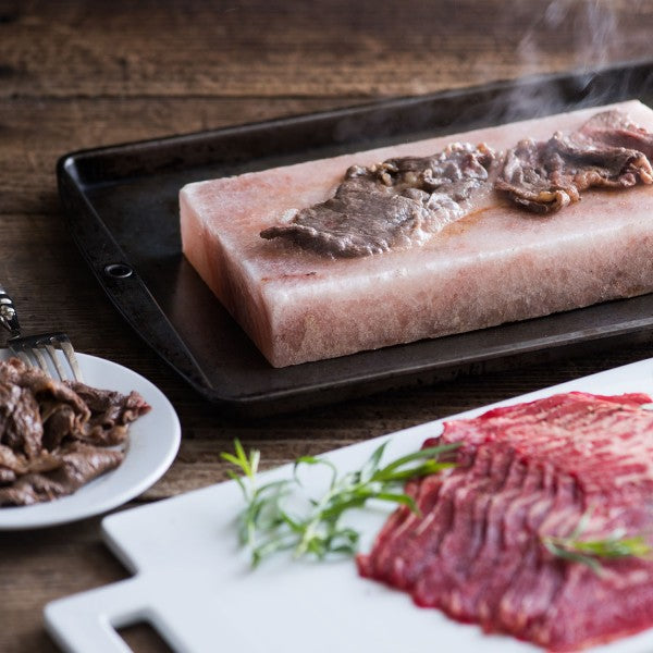 Raw beef on a salt block with sliced beef on a plate and cutting board.