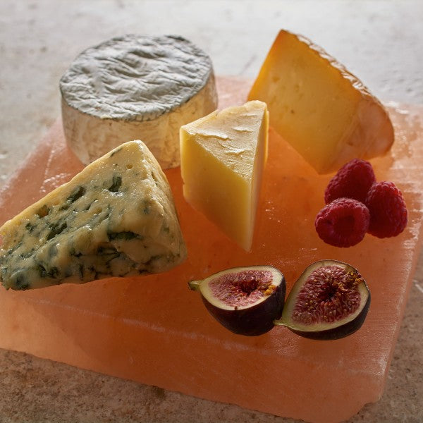 Assorted cheeses with figs and raspberries on a pink stone board.