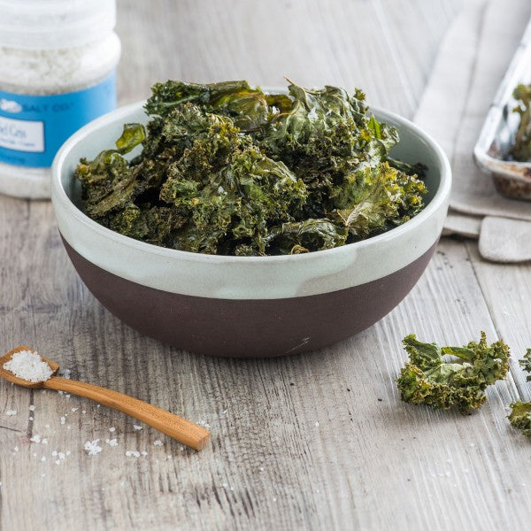 Bowl of kale chips on a wooden surface with a salt container.