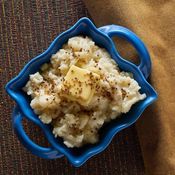 Mashed potatoes with a pat of butter in a blue bowl on a textured surface