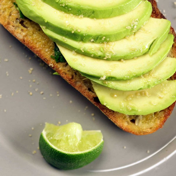 Avocado slices on toast with a lime wedge on a gray plate