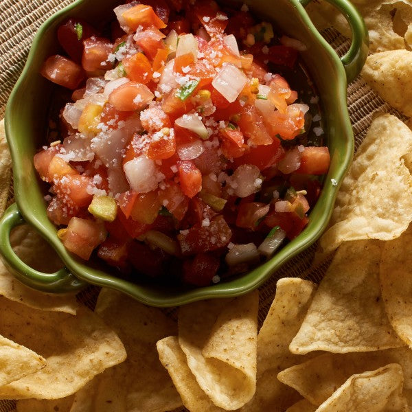 Green bowl of salsa with tortilla chips on a textured surface