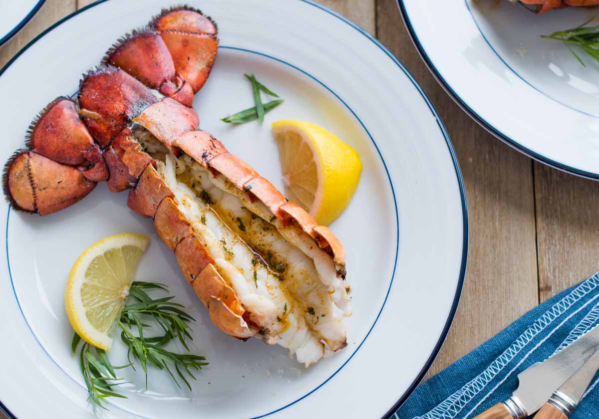 Lobster tail on a plate with lemon and herbs on a wooden table