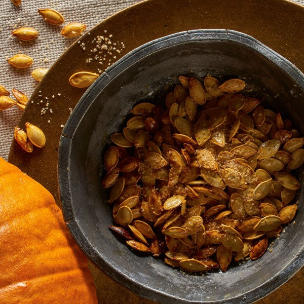 Roasted pumpkin seeds in a black bowl with a pumpkin on a wooden surface
