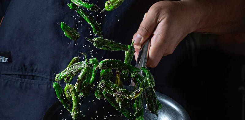 Man frying shishito peppers in pan with salt