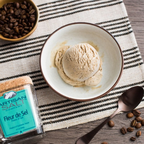 Bowl of coffee-flavored ice cream with coffee beans and Artisan Salt Company container on a striped fabric background