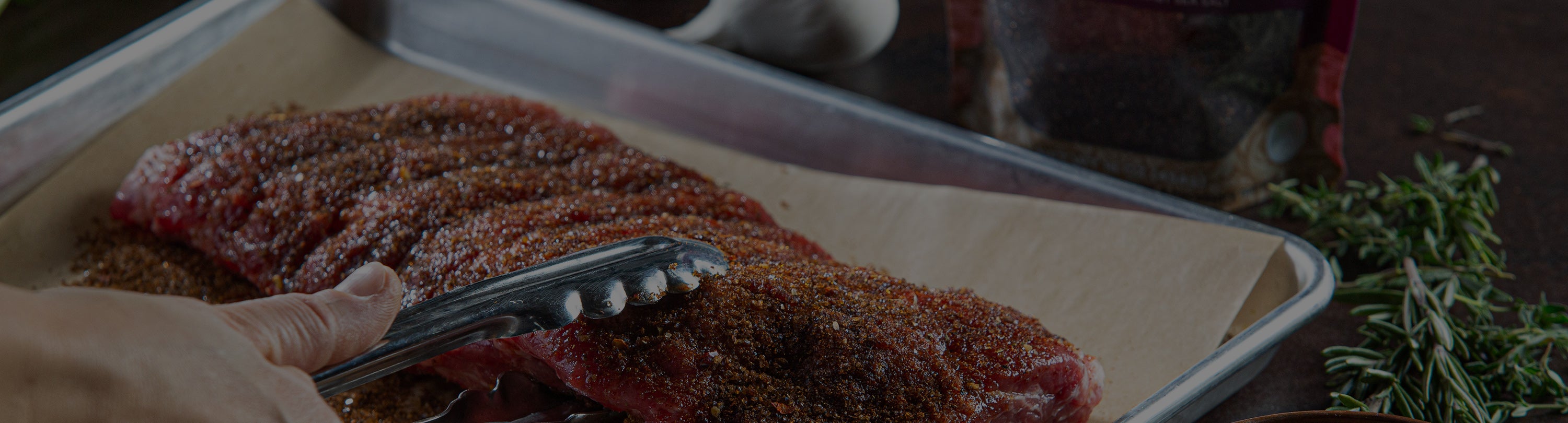 Raw meat being seasoned with a brush on a tray