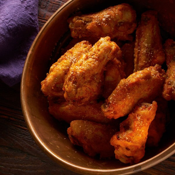 Bowl of chicken wings on a wooden surface with a purple cloth.