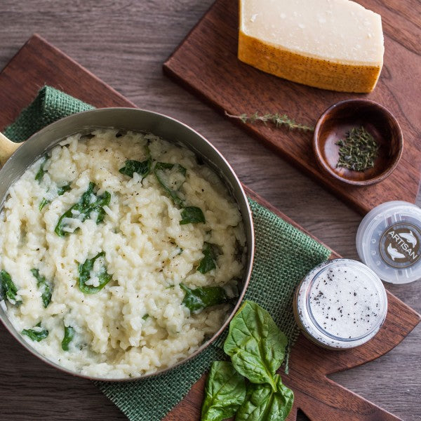 Risotto with spinach in a bowl on a wooden table with Parmesan cheese and herbs.