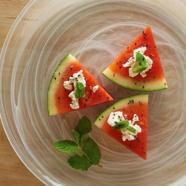 Three triangular slices of watermelon with feta cheese and mint leaves on a glass plate.